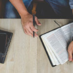 man holding a bible on table with journal and pen