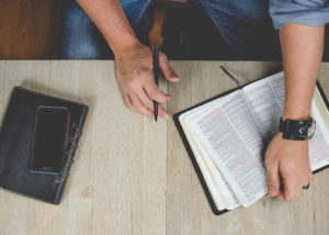 man holding a bible on table with journal and pen (Photo by Ben White on Unsplash)