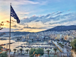 Greek flag in front of marina at sunset with city in background