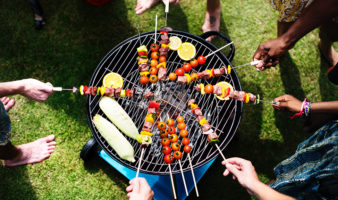 People standing around a small grill holding shish kabobs.