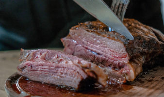 A knife cutting through rare cooked meat while a fork holds it.